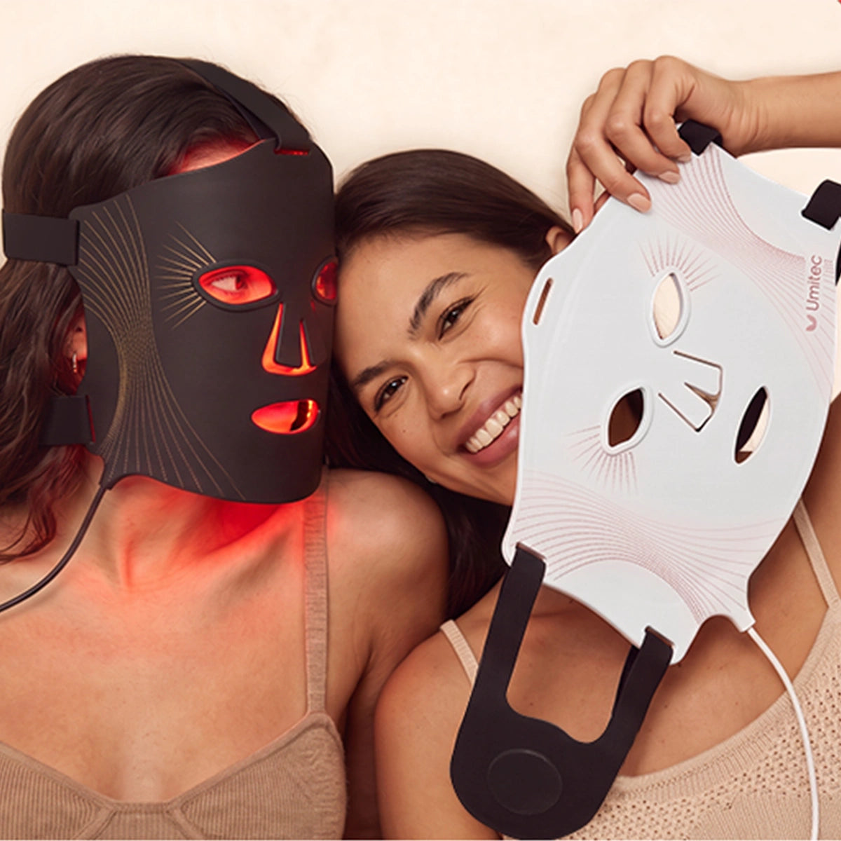 Two woman lean together, one wearing the black Umitec Led Face Mask, while one holding a white one