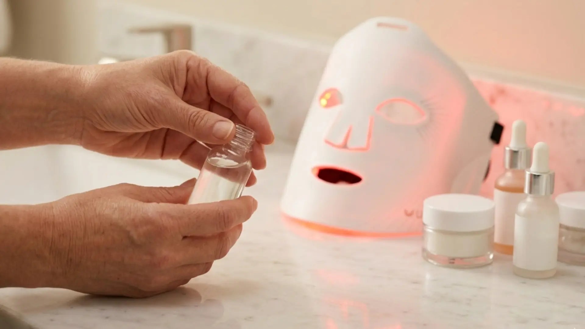 Skincare serums and a white LED face mask arranged on a marble vanity — a guide to using retinol, vitamin C, and hyaluronic acid safely with LED light therapy.